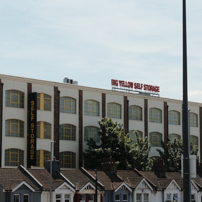 Exterior view of a multi-storey white building with large, arched yellow-framed windows, labelled as a self-storage facility with vertical black signage reading 'Self Storage' on the left side. The bu